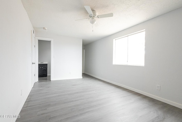 spare room with a textured ceiling, wood finished floors, a ceiling fan, and baseboards