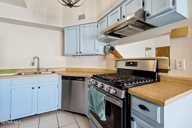 kitchen featuring extractor fan, appliances with stainless steel finishes, light tile patterned flooring, sink, and blue cabinetry