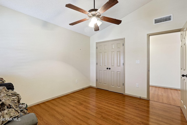 unfurnished bedroom with ceiling fan, a textured ceiling, vaulted ceiling, a closet, and light wood-type flooring