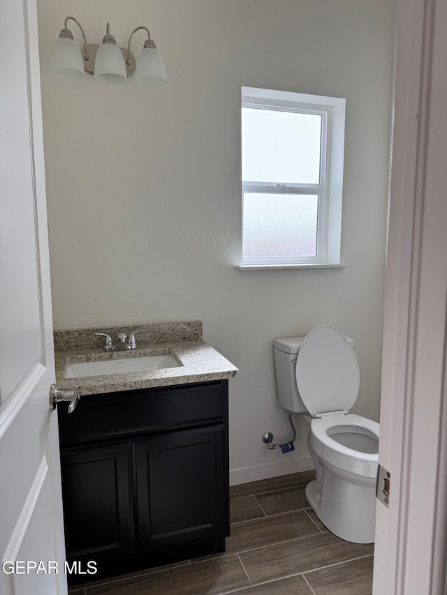 bathroom with baseboards, toilet, vanity, and wood finish floors