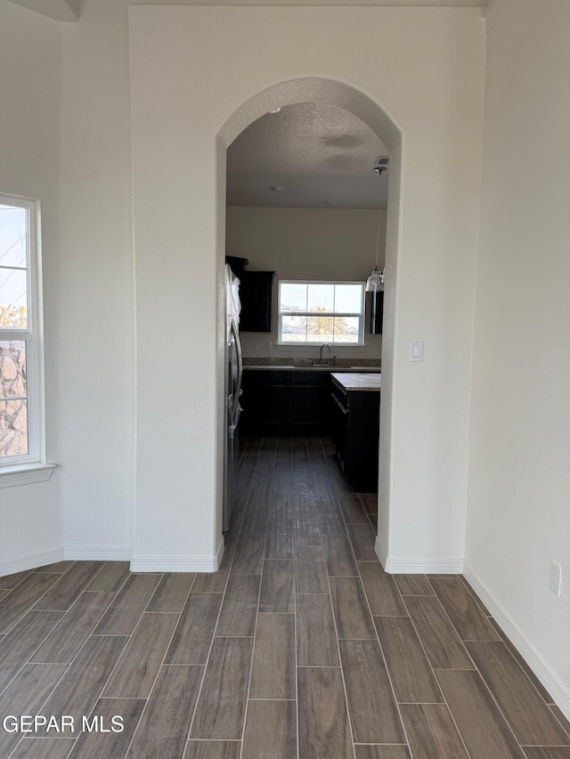 hall featuring baseboards, wood tiled floor, arched walkways, a textured ceiling, and a sink