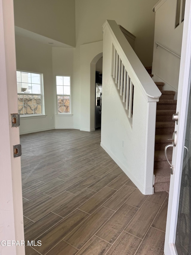 interior space with baseboards, wood finish floors, stairs, a towering ceiling, and arched walkways