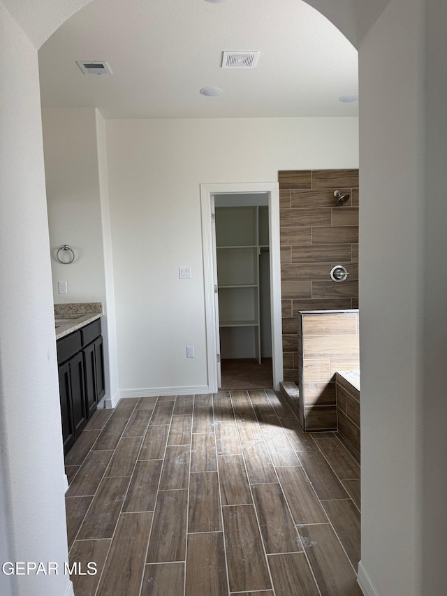 full bathroom featuring a spacious closet, baseboards, visible vents, and wood tiled floor