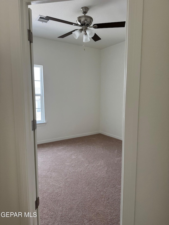 carpeted spare room featuring visible vents, baseboards, and ceiling fan