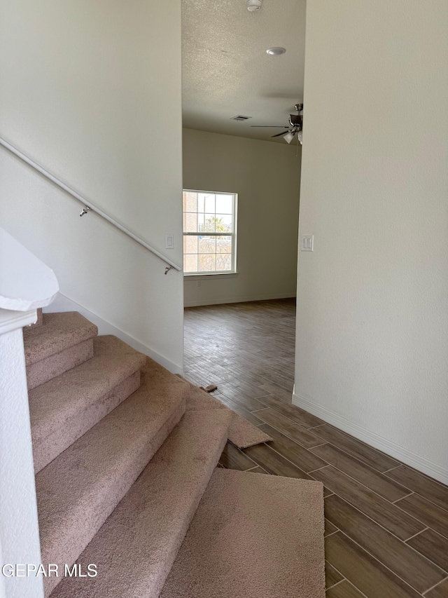 stairs featuring visible vents, a textured ceiling, baseboards, ceiling fan, and wood tiled floor