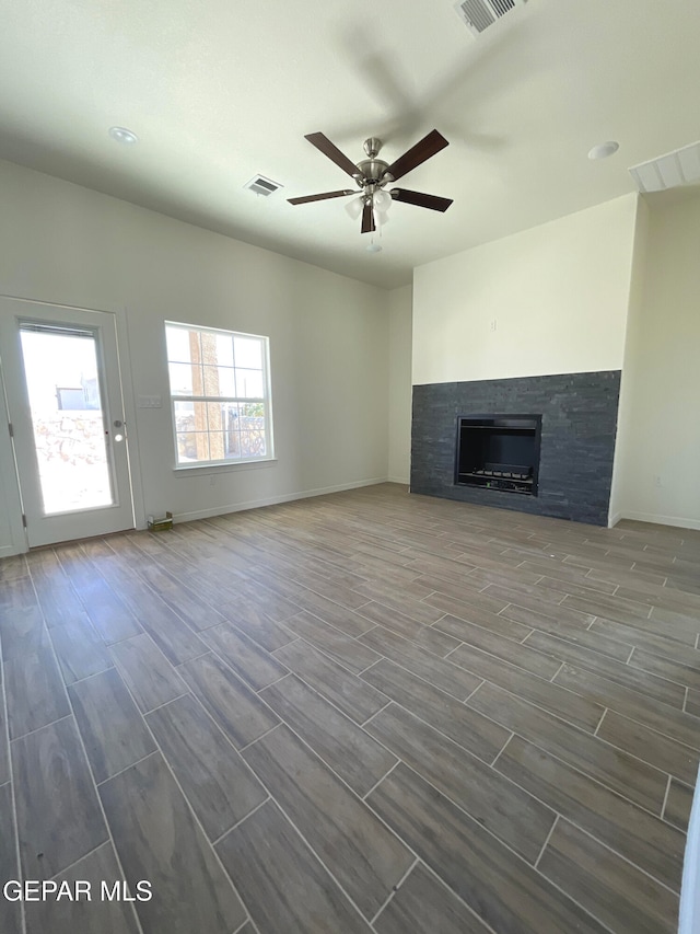 unfurnished living room featuring a glass covered fireplace, a ceiling fan, visible vents, and wood finish floors