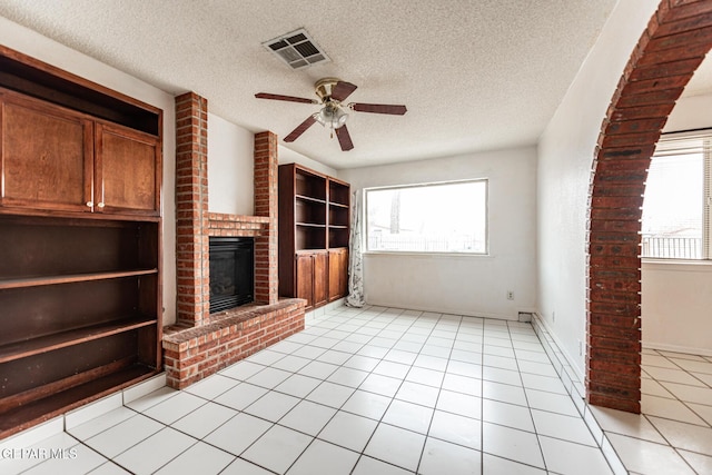 unfurnished living room featuring a brick fireplace, light tile patterned floors, a textured ceiling, and ceiling fan