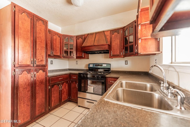 kitchen featuring stainless steel gas range, sink, custom exhaust hood, a textured ceiling, and light tile patterned floors