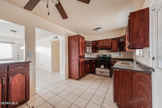 kitchen with sink, custom exhaust hood, stainless steel gas range oven, light tile patterned floors, and ceiling fan