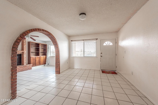 tiled foyer entrance featuring ceiling fan, a brick fireplace, and a textured ceiling