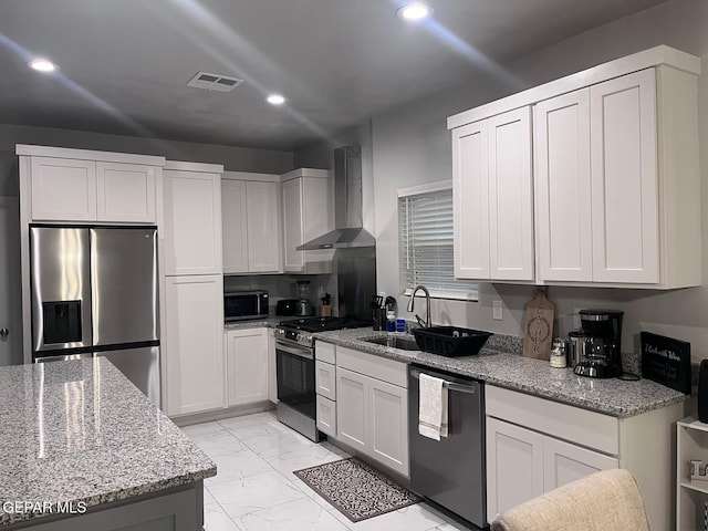 kitchen featuring sink, appliances with stainless steel finishes, white cabinets, light stone countertops, and wall chimney range hood