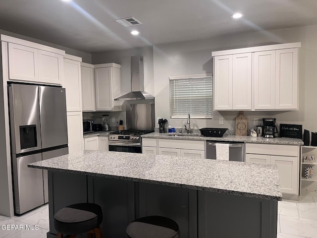 kitchen featuring wall chimney exhaust hood, white cabinetry, stainless steel appliances, and light stone countertops