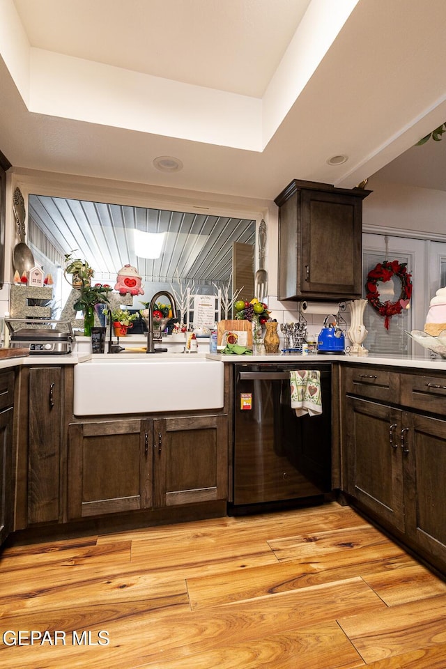 kitchen with dark brown cabinetry, black dishwasher, sink, and light wood-type flooring