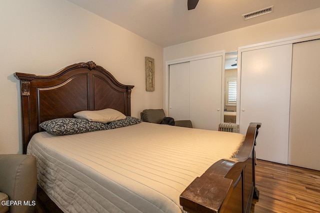 bedroom featuring radiator, two closets, hardwood / wood-style floors, and ceiling fan