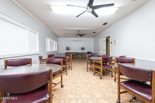 interior space with light tile patterned floors, ceiling fan, a textured ceiling, and brick wall