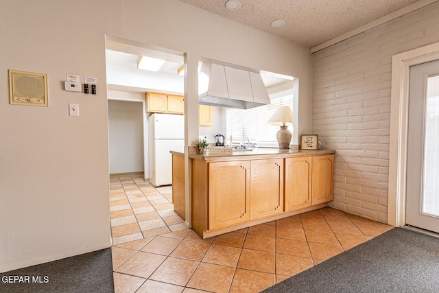 kitchen featuring a textured ceiling, light tile patterned floors, kitchen peninsula, white fridge, and brick wall