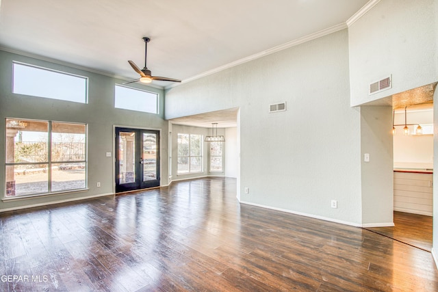 unfurnished living room featuring crown molding, ceiling fan with notable chandelier, dark wood-type flooring, and a towering ceiling