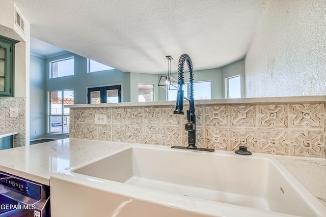 interior details with dishwashing machine, sink, pendant lighting, light stone counters, and a textured ceiling