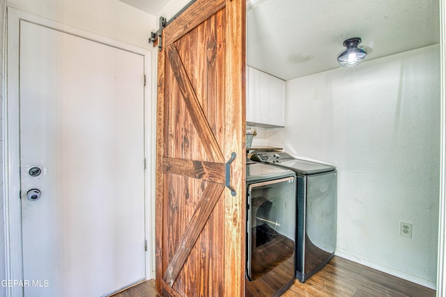 clothes washing area featuring hardwood / wood-style floors, cabinets, independent washer and dryer, a barn door, and a textured ceiling