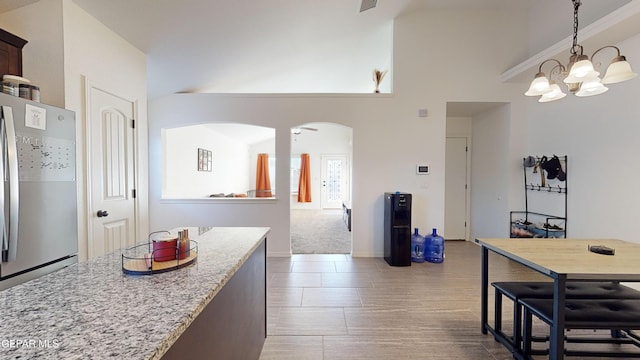 kitchen with dark brown cabinetry, light stone counters, a chandelier, hanging light fixtures, and stainless steel fridge