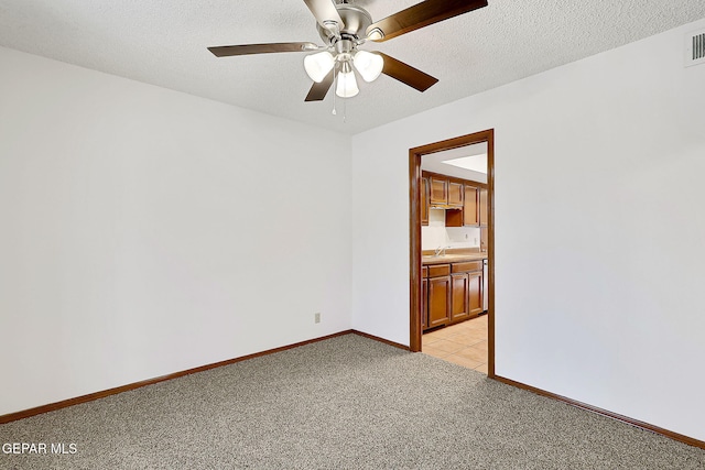 spare room featuring ceiling fan, light colored carpet, sink, and a textured ceiling