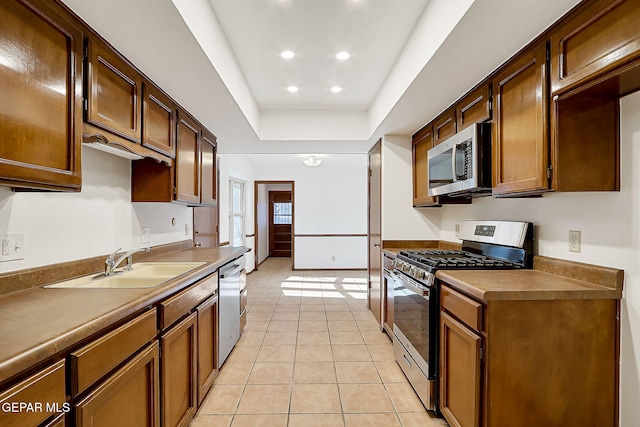 kitchen featuring appliances with stainless steel finishes, a tray ceiling, sink, and light tile patterned floors