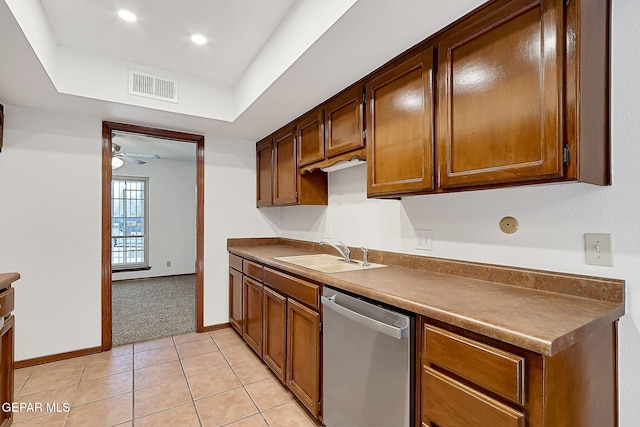 kitchen featuring sink, light tile patterned floors, dishwasher, ceiling fan, and a tray ceiling