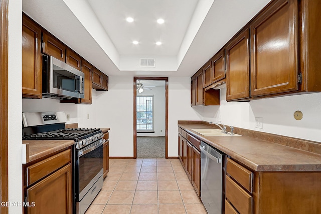 kitchen featuring light tile patterned flooring, sink, a raised ceiling, ceiling fan, and stainless steel appliances