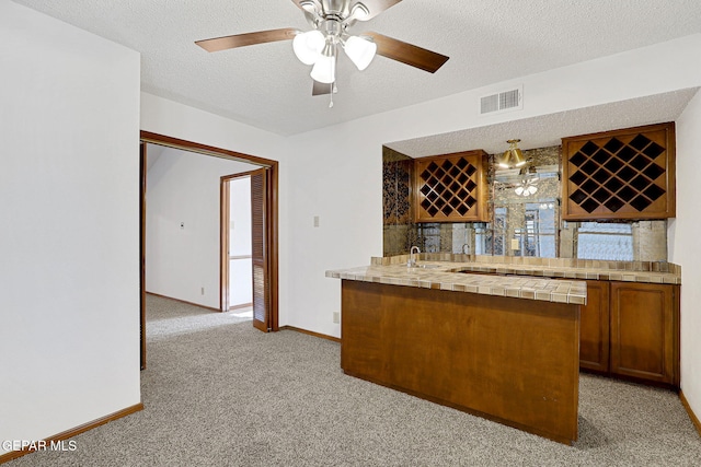 bar with light carpet, ceiling fan, tile countertops, and a textured ceiling