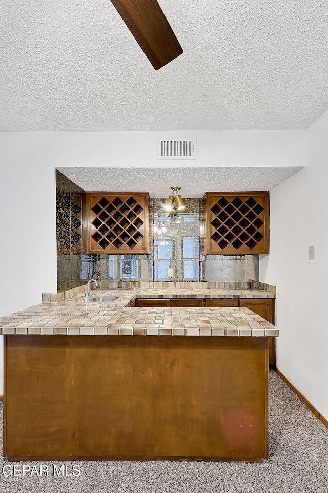 bar with light carpet, sink, tile countertops, and a textured ceiling