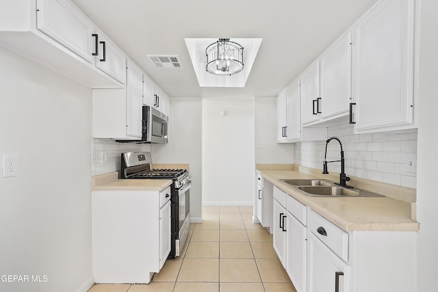 kitchen featuring sink, light tile patterned floors, stainless steel appliances, a notable chandelier, and white cabinets