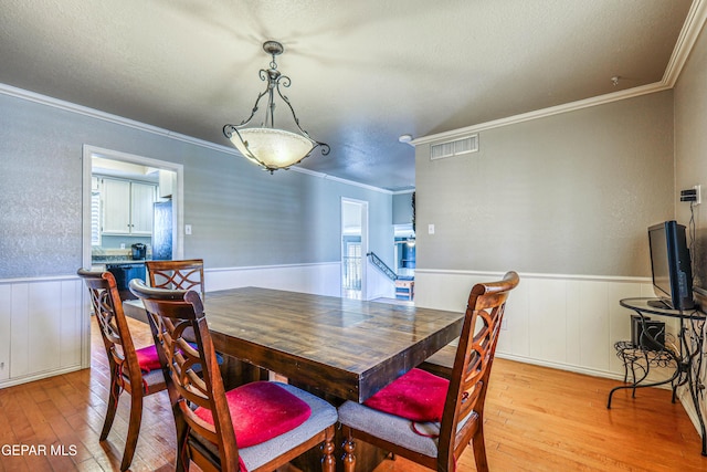 dining space with crown molding, a textured ceiling, and light hardwood / wood-style flooring