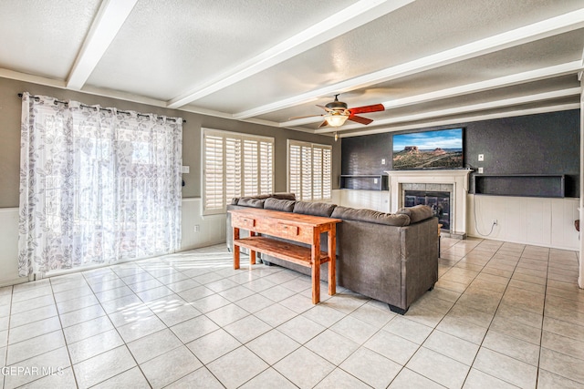 tiled living room with beam ceiling, a tiled fireplace, ceiling fan, and a textured ceiling