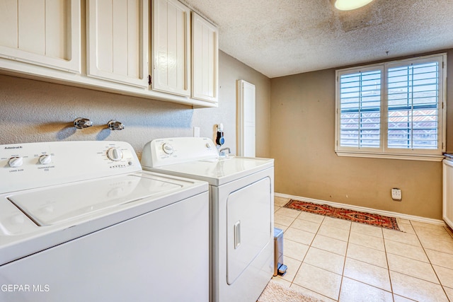 clothes washing area with light tile patterned flooring, cabinets, washing machine and dryer, and a textured ceiling