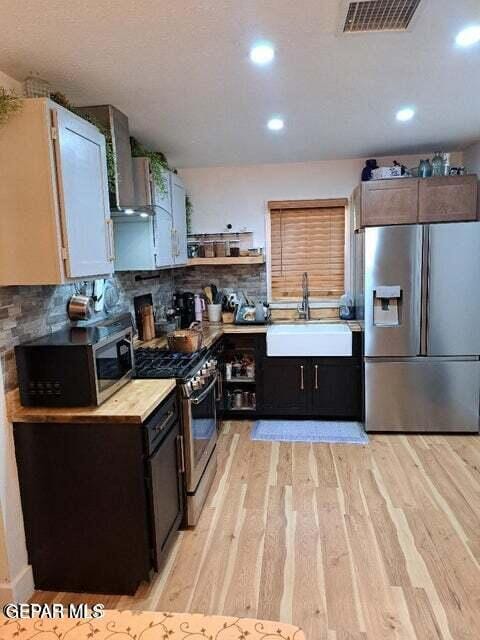 kitchen featuring sink, decorative backsplash, stainless steel appliances, wall chimney range hood, and light hardwood / wood-style flooring