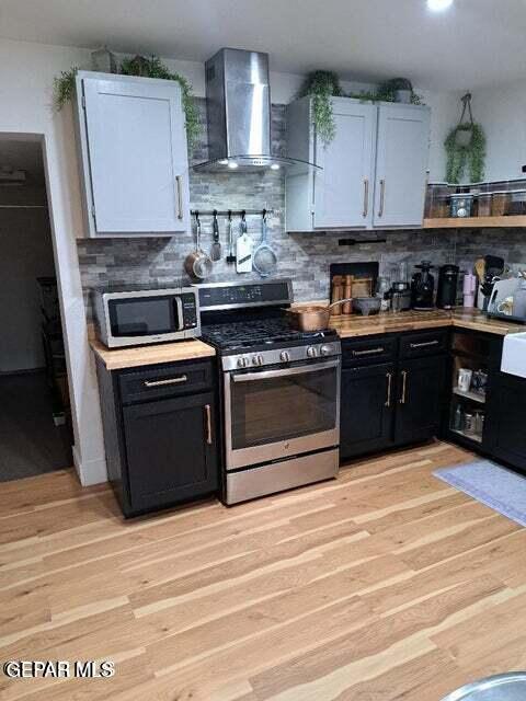 kitchen featuring stainless steel appliances, light wood-type flooring, wall chimney range hood, and white cabinets