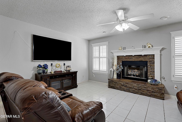 living room featuring ceiling fan, a fireplace, a textured ceiling, and light tile patterned floors