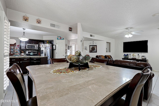 tiled dining space with a textured ceiling and ceiling fan