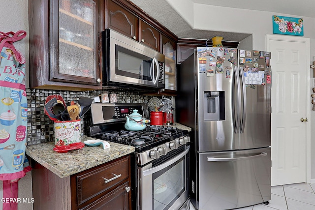 kitchen featuring light tile patterned flooring, appliances with stainless steel finishes, decorative backsplash, light stone counters, and dark brown cabinets