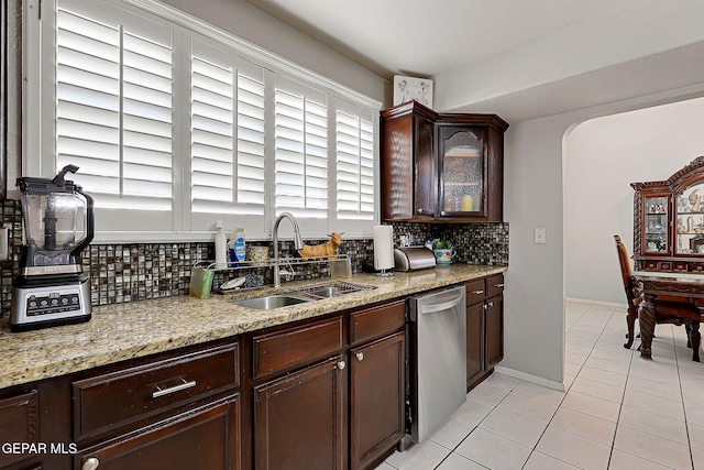 kitchen featuring sink, backsplash, stainless steel dishwasher, light tile patterned floors, and dark brown cabinets