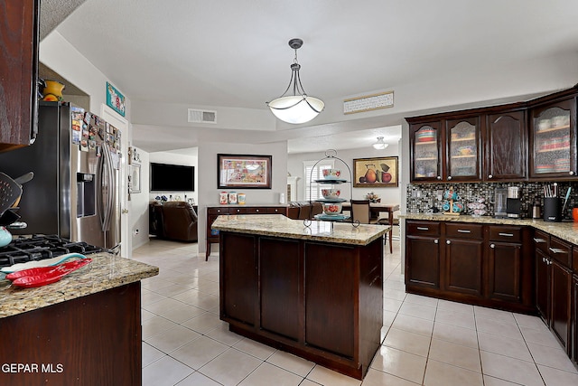 kitchen featuring light stone counters, dark brown cabinets, stainless steel fridge, a kitchen island, and pendant lighting