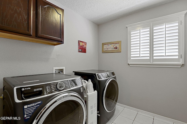 clothes washing area with cabinets, light tile patterned floors, a textured ceiling, and washing machine and clothes dryer