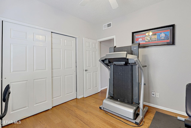 exercise area featuring ceiling fan, a textured ceiling, and light wood-type flooring