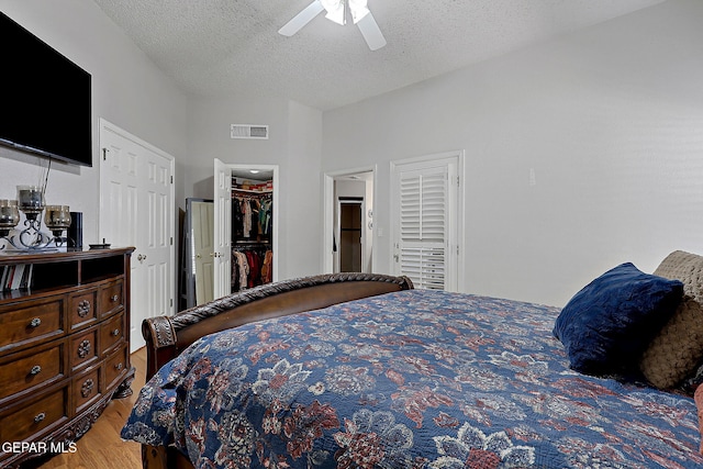 bedroom featuring ceiling fan, a walk in closet, light hardwood / wood-style flooring, and a textured ceiling