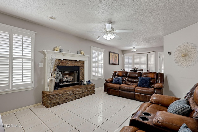 living room with ceiling fan, a fireplace, a textured ceiling, and light tile patterned floors