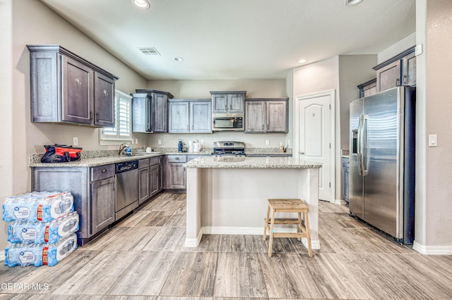 kitchen with a breakfast bar area, stainless steel appliances, a center island, dark brown cabinetry, and light stone countertops