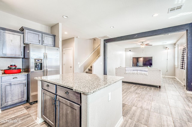 kitchen featuring light stone counters, stainless steel fridge with ice dispenser, dark brown cabinets, a kitchen island, and ceiling fan