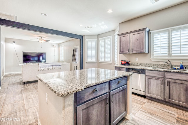 kitchen featuring ceiling fan, dark brown cabinetry, light stone countertops, a kitchen island, and stainless steel dishwasher