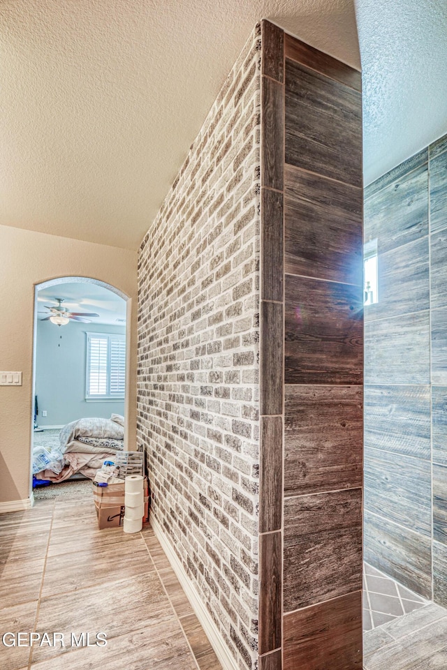 hallway with wood-type flooring, brick wall, and a textured ceiling