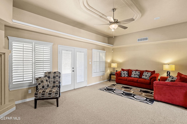 carpeted living room with a tray ceiling, french doors, and ceiling fan